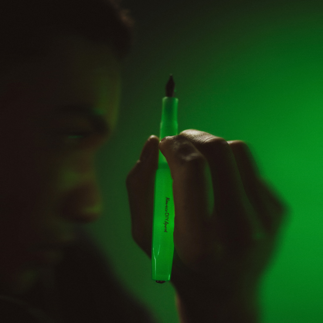 Person holding a green Kaweco DIY Sport Glow pen against a dark background